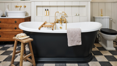 black and white checkerboard floor bathroom witha freestanding black bath with a wooden bath tray and a small stool next to it