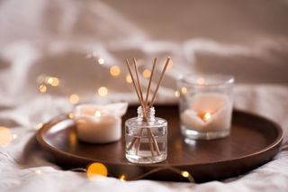 A wooden tray with a reed diffuser with two cream candles and fairy lights.