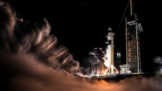 a white and black spacex rocket ignites its engines on the launch pad at night, without leaving the ground.