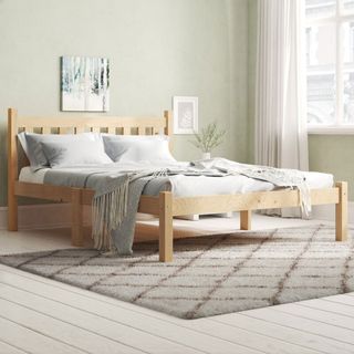 Wooden bed frame with grey bedding in a light grey room and a furry grey carpet on a white wooden floor