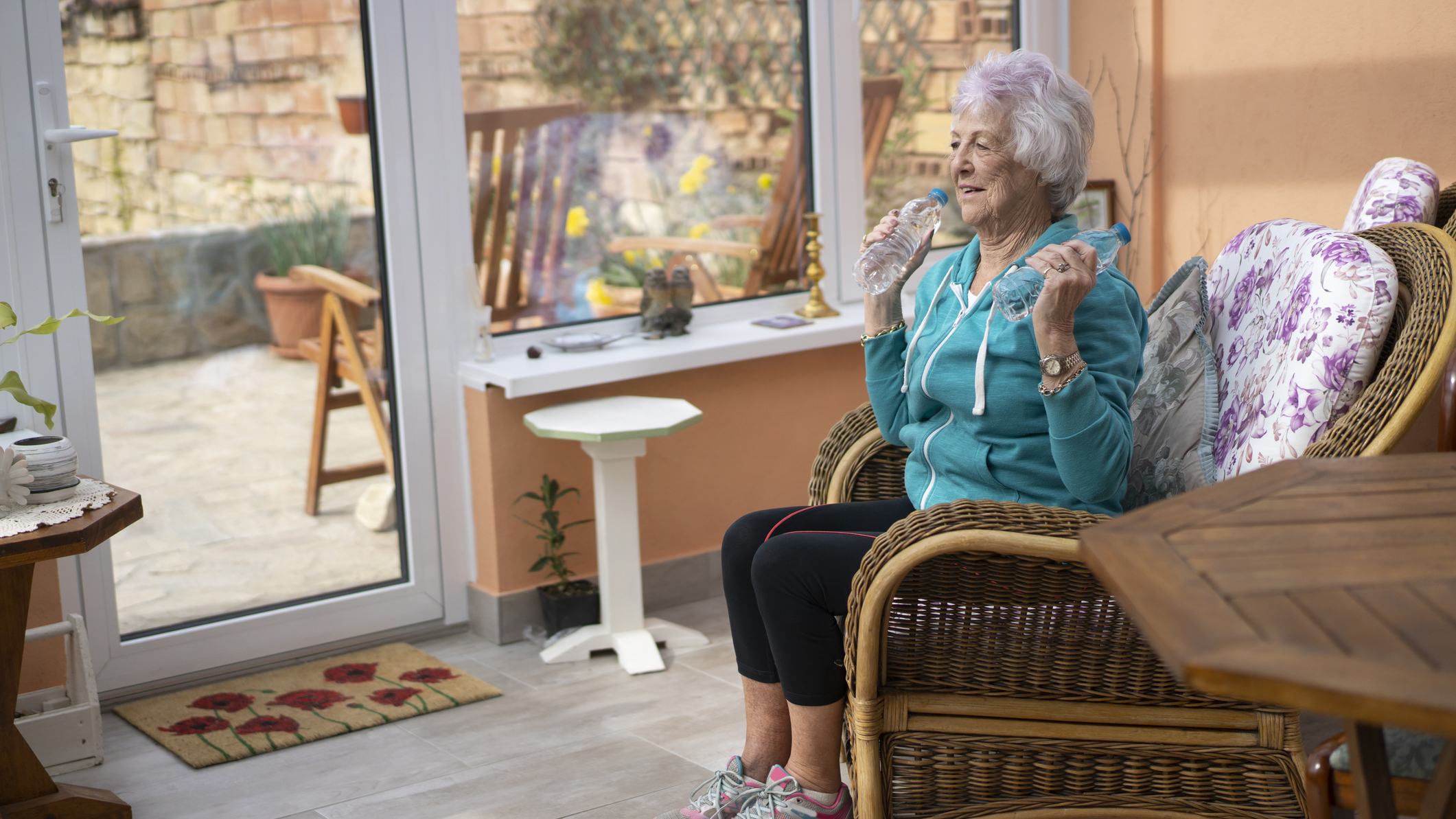Senior woman sitting in chair holding filled water bottles by her shoulders