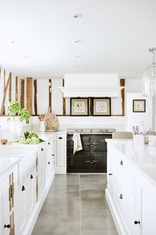 Modern kitchen with white surfaces, walls and cabinets and a striking traditional, black stove and bare wood, as an example of kitchen renovation cost.