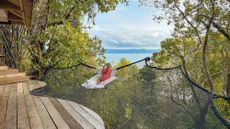 A woman sits on a net outside her room at Somewhere Only We Know Resort in Thailand that overlooks the water