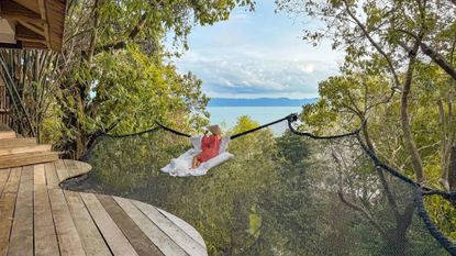 A woman sits on a net outside her room at Somewhere Only We Know Resort in Thailand that overlooks the water