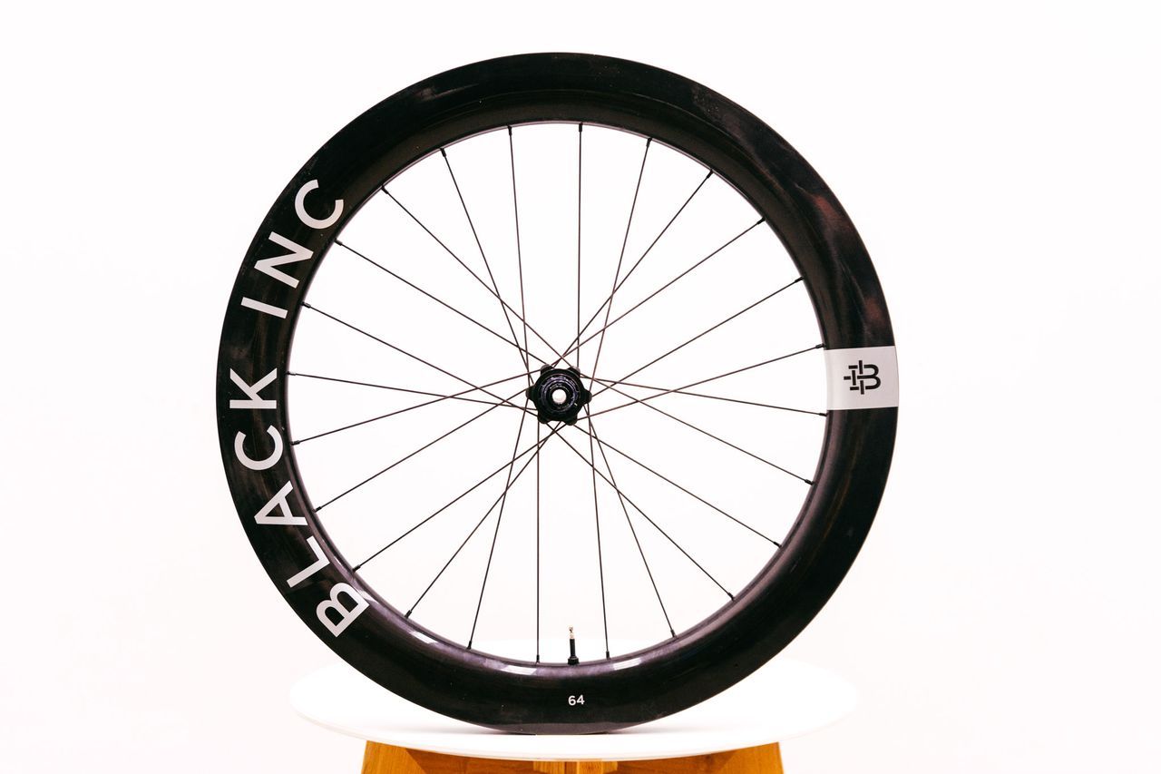 A Black Inc 64 Gravel wheel stands on a chair