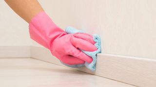 person with a pink glove on cleaning baseboards with a microfiber cloth
