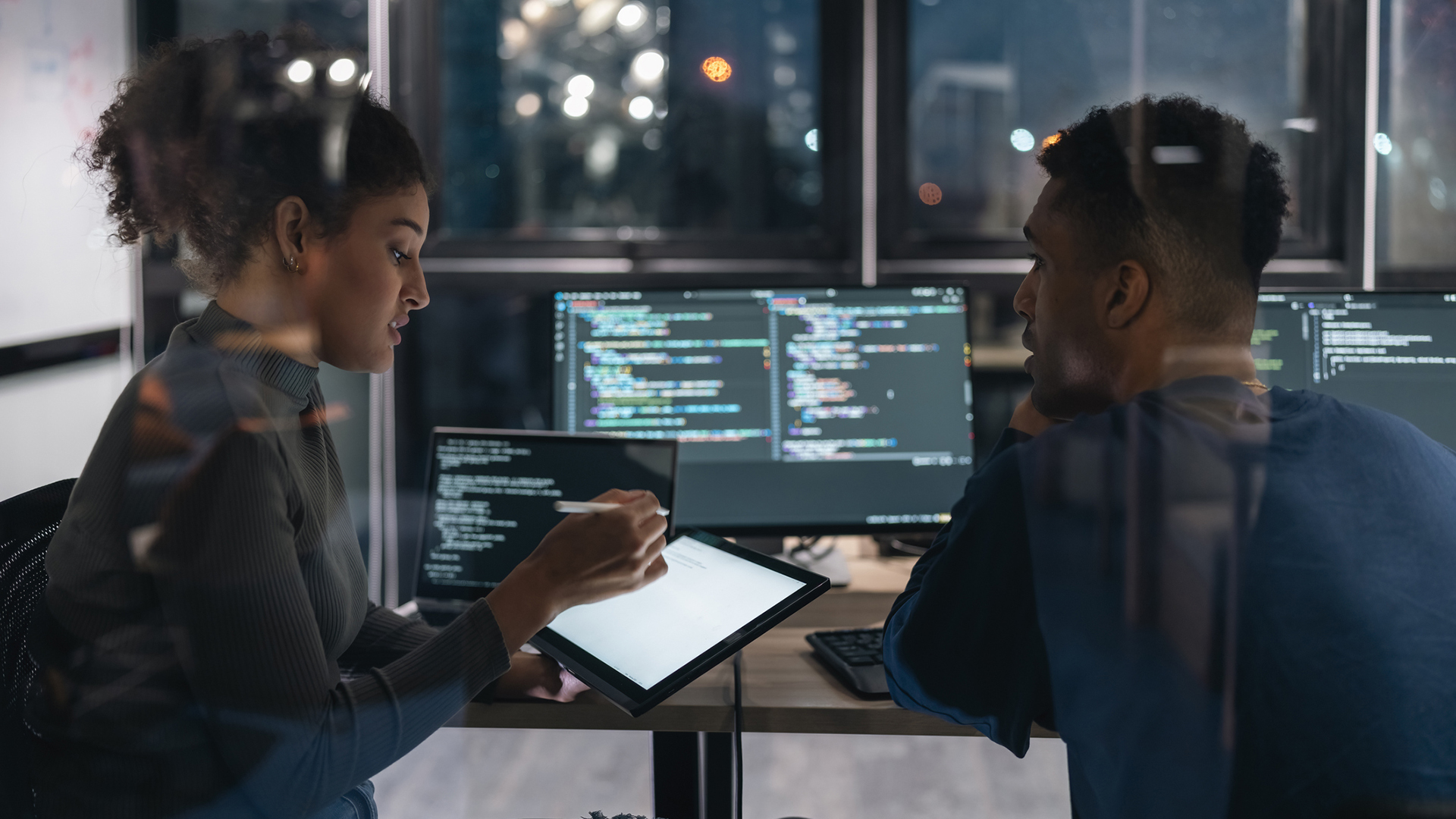 Two Software developers in modern office collaborating analysing the coding on computer screen.