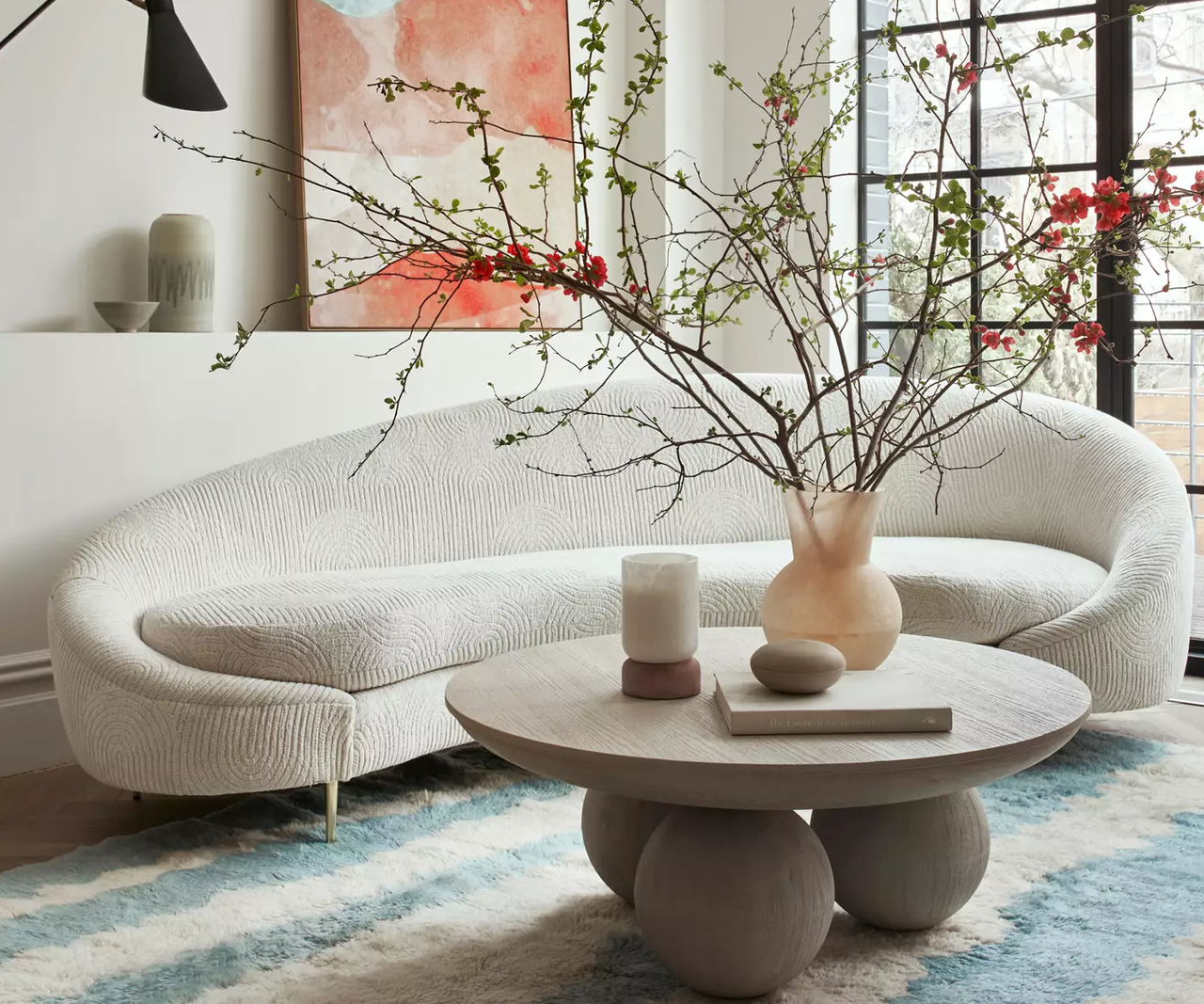 A living room with a curved sofa, a blue and white rug, and a coffee table with oversized bun feet