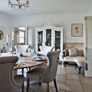 A neutral dining room with a chandelier and white ornate dresser