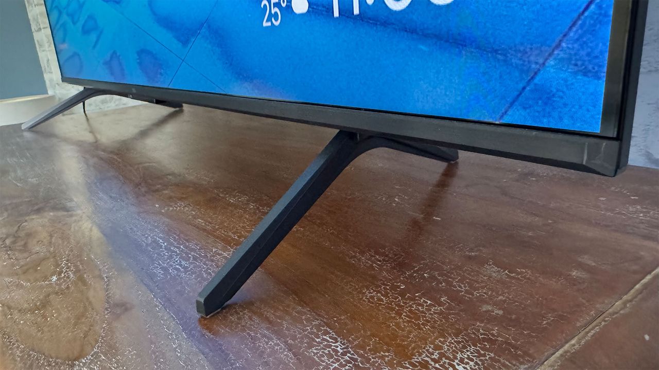 A close-up of the feet of the TCL C6KS 50-inch TV on a wooden surface.