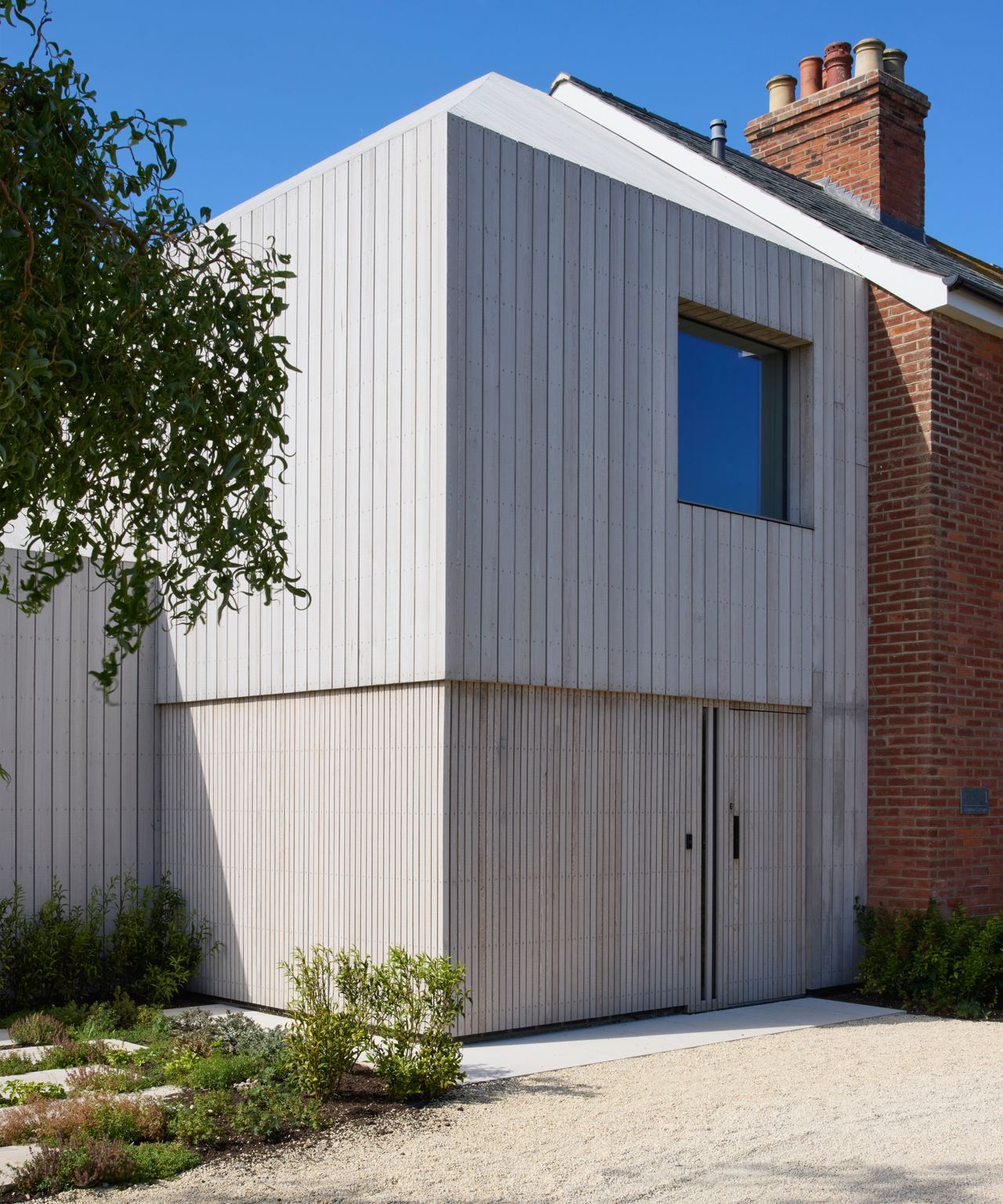 exterior of double and single storey timber frame extension on side of brick property, clad in weathered vertical timber cladding