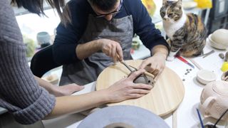 a person teaches pottery making while a cat sits and watches