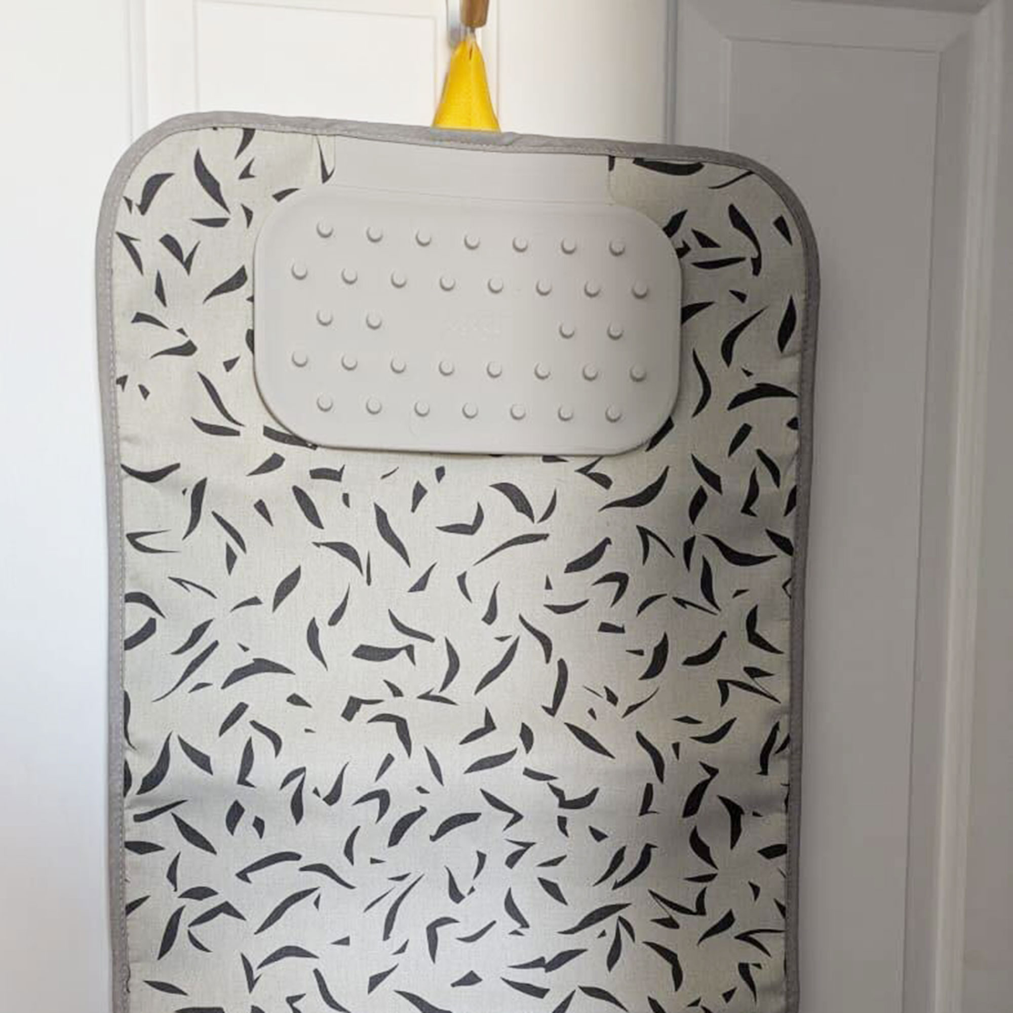 Grey patterned ironing mat hanging up on door