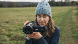 The Canon XA75 camcorder held by a woman in a hat on a field