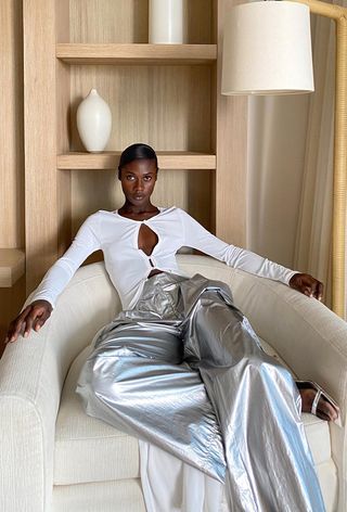 a casual party outfit with a woman sitting down wearing a white cardigan top with silver jeans and silver sandals