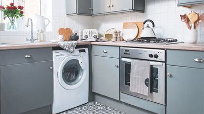 Grey kitchen with tiled floor, wooden countertops, and a white washing machine