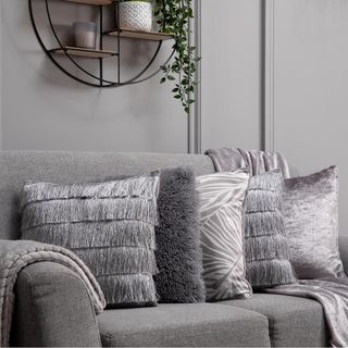 Grey couch with grey cushions and throw against grey wall