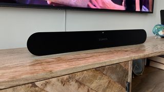 The Sonos Ray soundbar on a wooden TV cabinet under a TV.