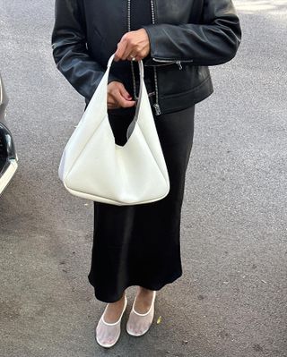 Dawn Tan wearing a leather jacket, black skirt, white bag, and white Dear Frances mesh flats.
