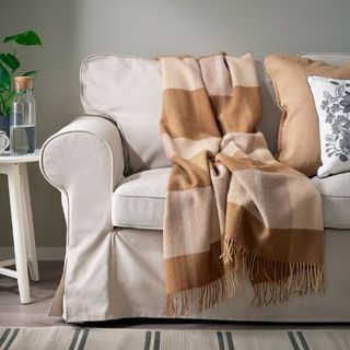 cream sofa with brown cushion and checked blanket