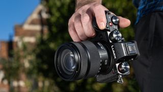 Panasonic Lumix S5D mirrorless camera with a lens attached, held in one hand by the camera grip in strong sunshine