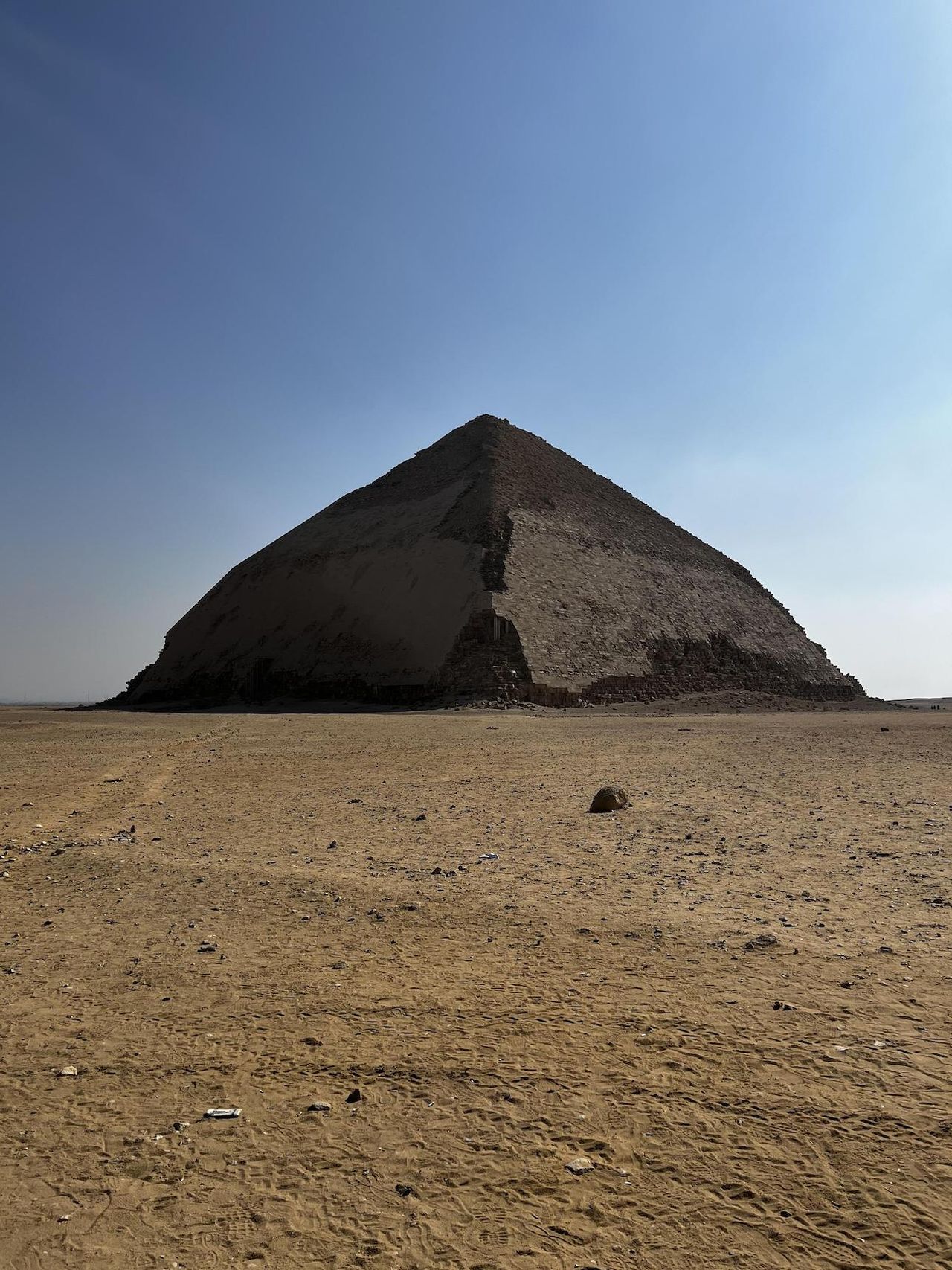 A pyramid made of stone in the desert. The shape is more rounded and the top is at a lower angle than the bottom, giving it a "bent" shape