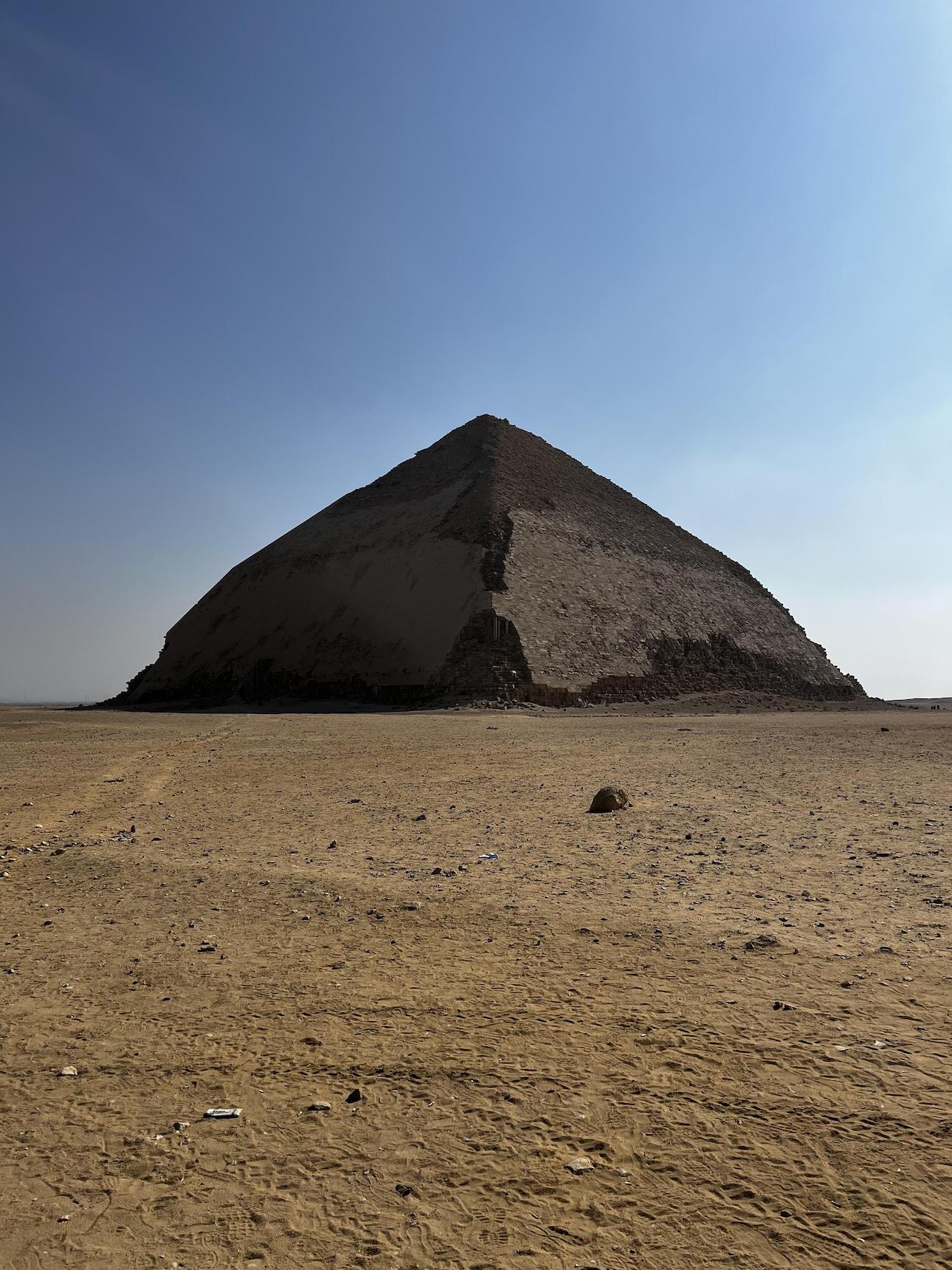 A pyramid made of stone in the desert. The shape is more rounded and the top is at a lower angle than the bottom, giving it a 