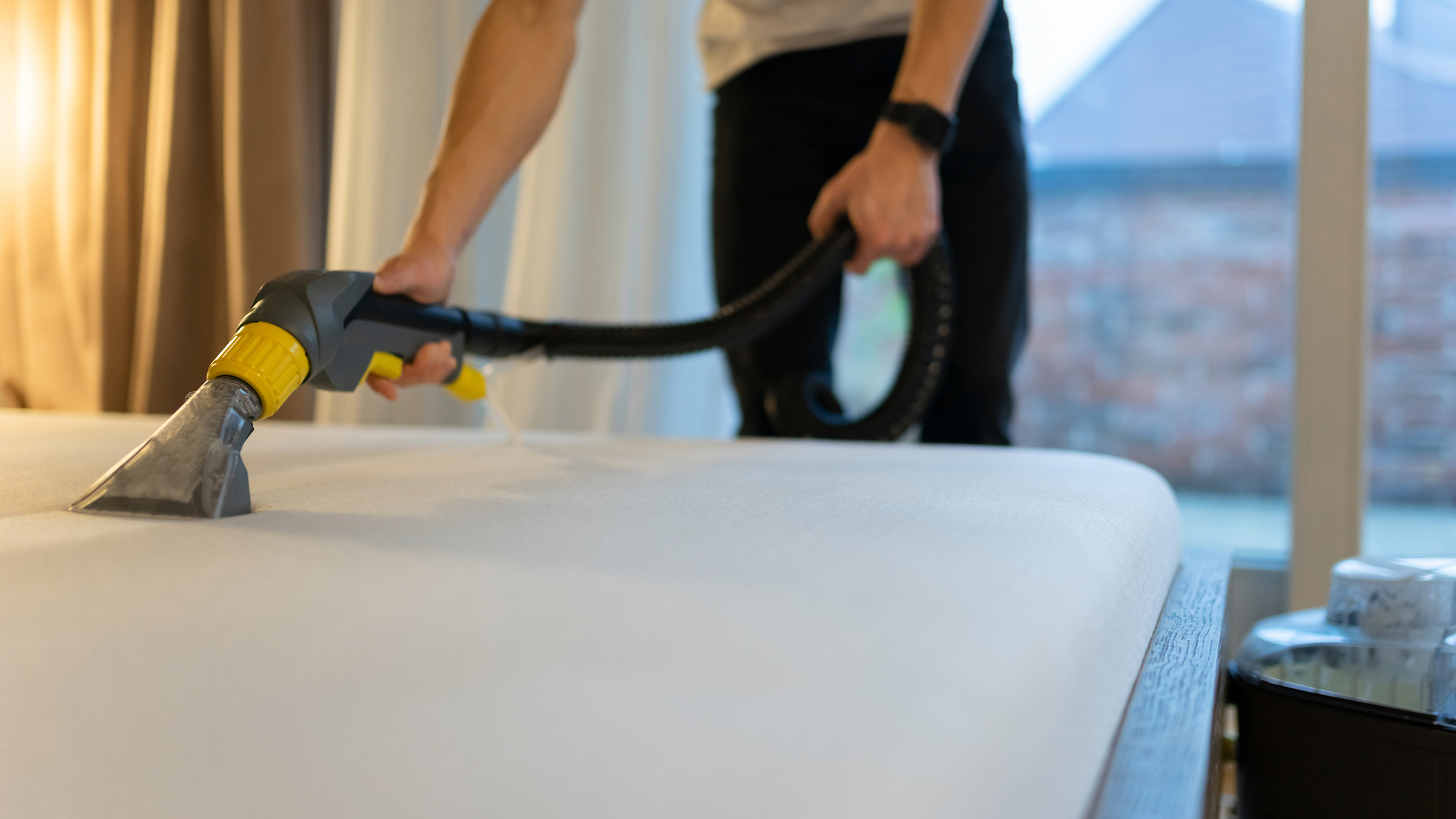 A man cleans a mattress using a handheld vacuum cleaner