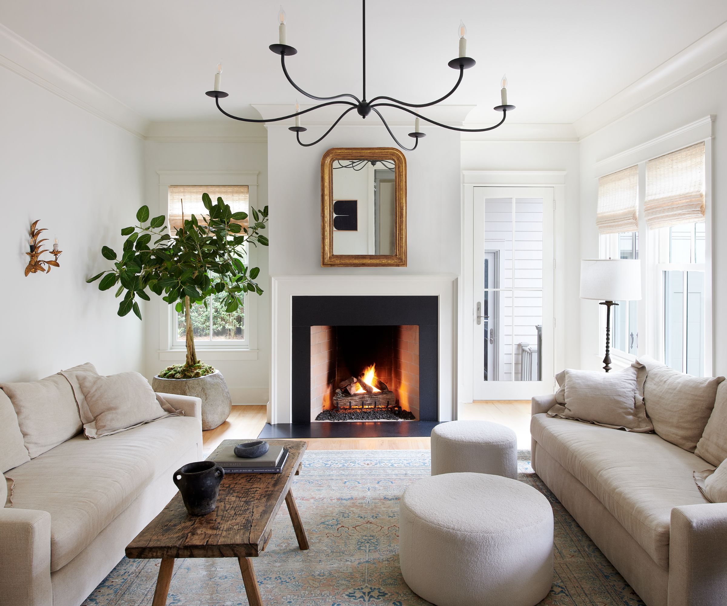 A white living room with white walls and ceiling, two light beige sofas, a vintage wooden coffee table, a neutral rug, and transitional decor.