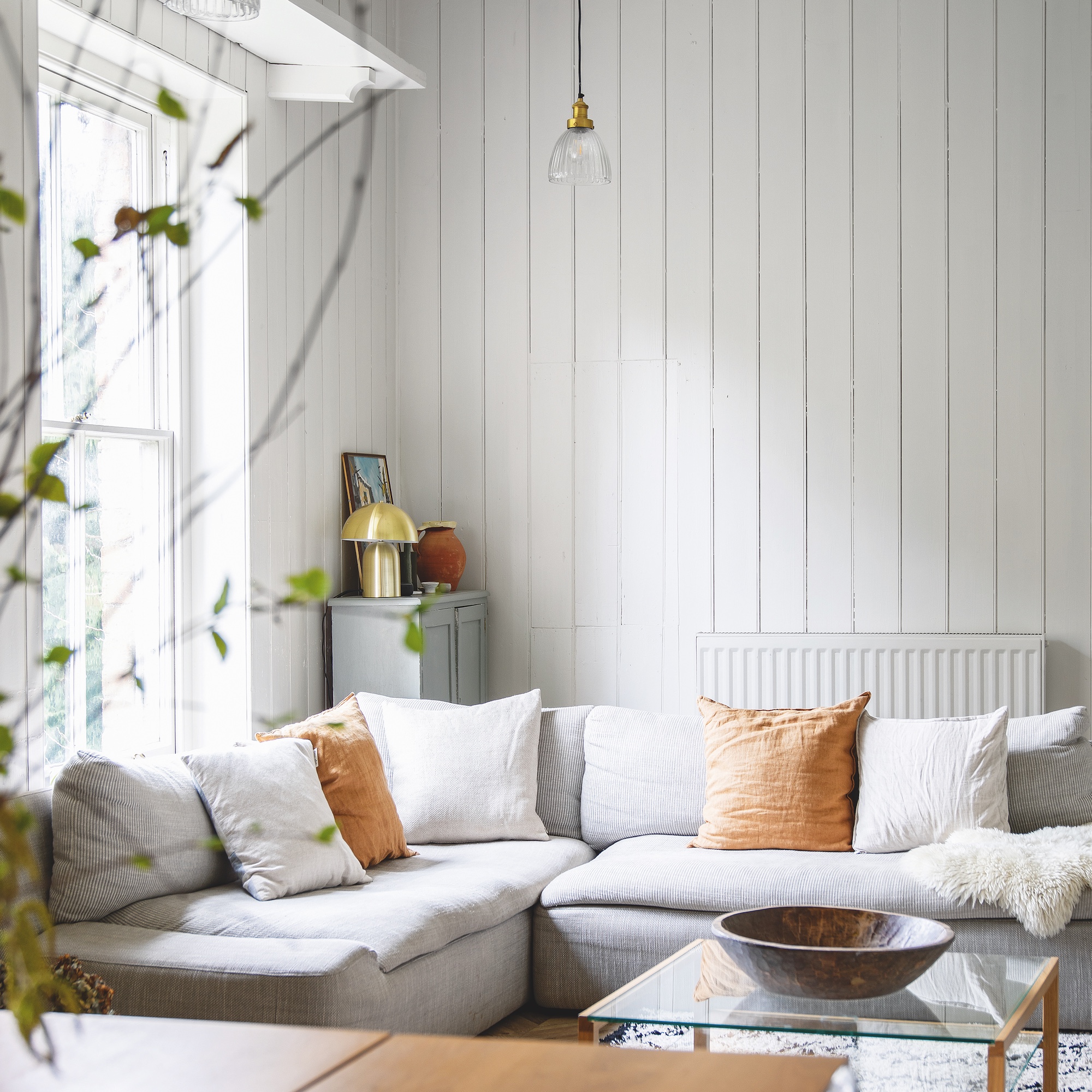 sitting room with wood panelled walls and pale grey corner sofa with square cushions