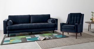 Made.com blue velvet sofa in a white living space with two rugs on the floor
