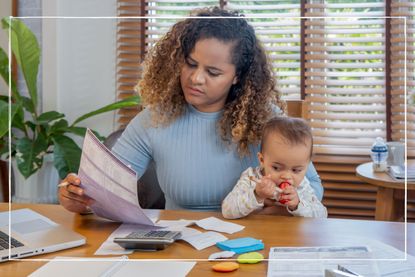 Working mum looking at bank account statement while holding her infant child on her lap