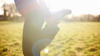 Woman standing on grassy field, stretching one leg behind her after finishing running early in the morning