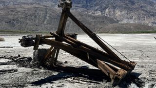 A wooden structure is toppled over on flat white ground. Dark mountains are in the background. Saline Valley Salt Tram tower on the ground