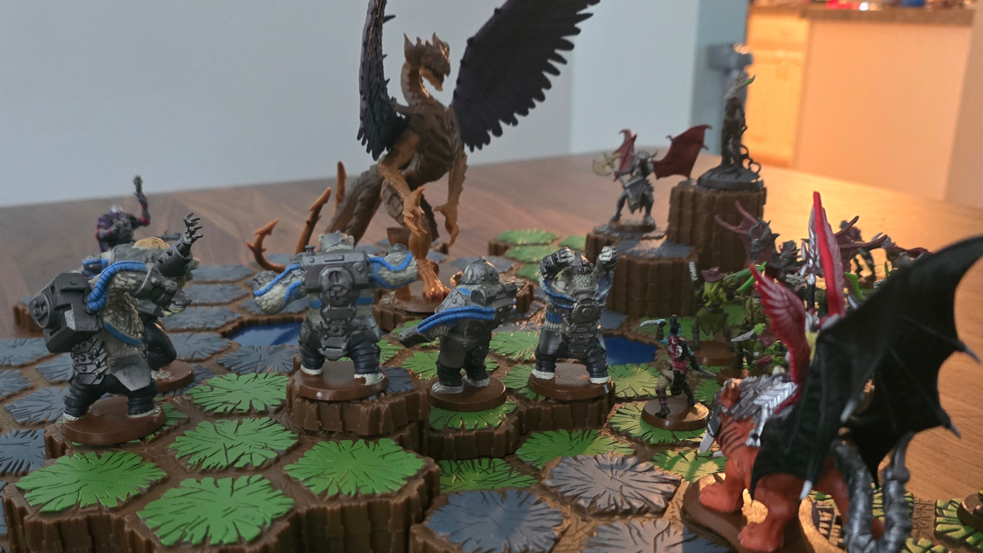An array of models including a dragon face each other on hexagonal map tiles, all on a wooden table