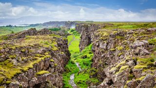 A green rocky landscape reveals the rift between two tectonic plates