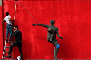 Workers painting at the Estadio Arsenio Erico in Paraguay in 2021, with a statue of the legendary player in the foreground.