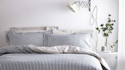 A blakc and white striped bedlinen set on a bed in a white bedroom with a vase of flowers on the bedside table