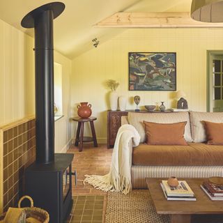 barn conversion living area with brown and white striped sofas, low wooden coffee able and large woodburning stove with chimney