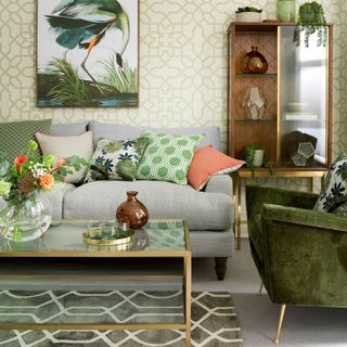 Sitting area with sofa and green velvet accent chair, brass and glass coffee table, patterned rug with large bird print on the wall