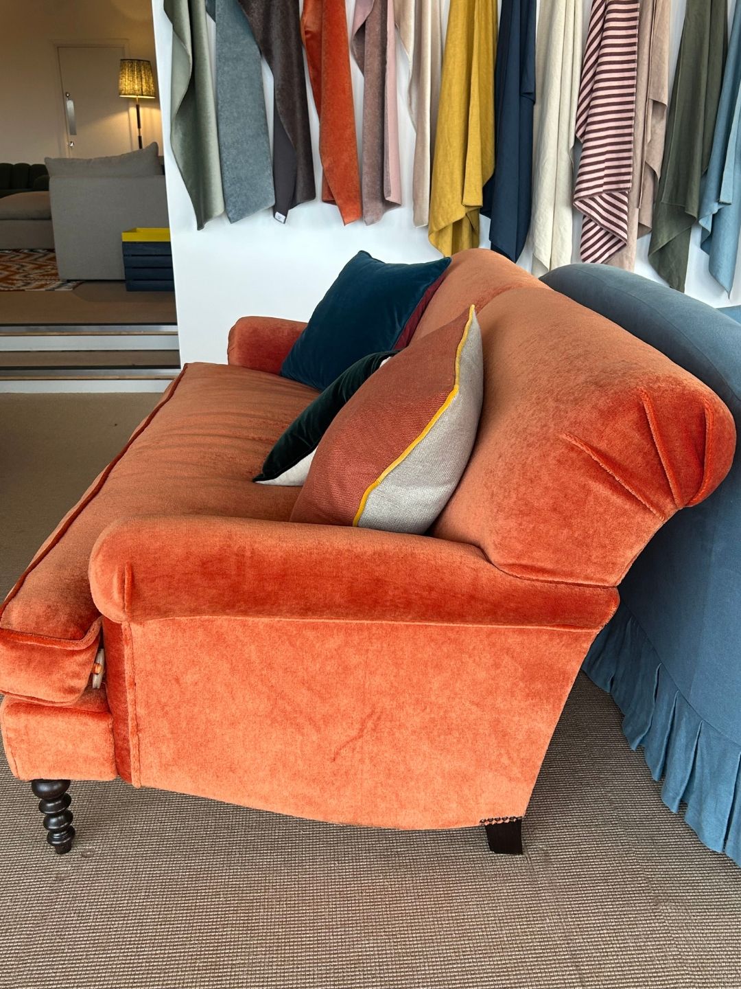 Side view of Schplendid's Ablion sofa in Marmalade Mohair, showing its gently curved armrest, plump back cushions and dark turned wooden legs.