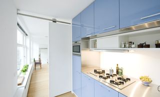 Kitchen area with white walls, ceilings and a sliding white door. Light blue cabinets with silver handles on the right.