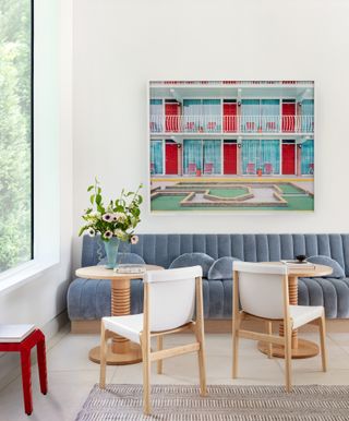 Light blue textured banquette with two cocktail tables, white chairs and a framed artwork piece