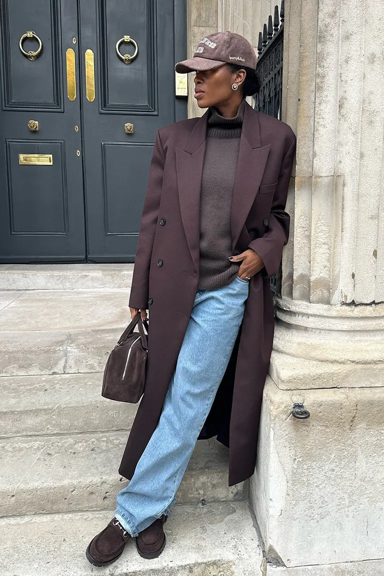 Woman in dark brown sweater, jeans, and bag.