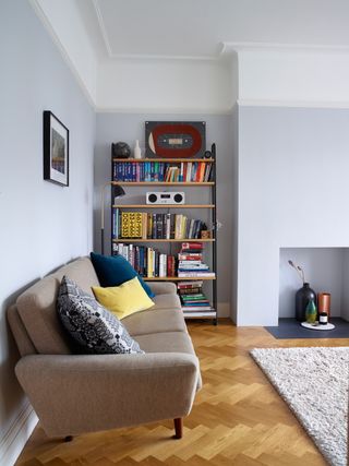 modern living room with a grey sofa, light walls, parquet flooring and open shelving