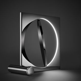 Alternative view of the chrome-plated 'Moonsetter' floor lamp that features a rotating metal disc that mimics the moon. It is pictured against a dark coloured background