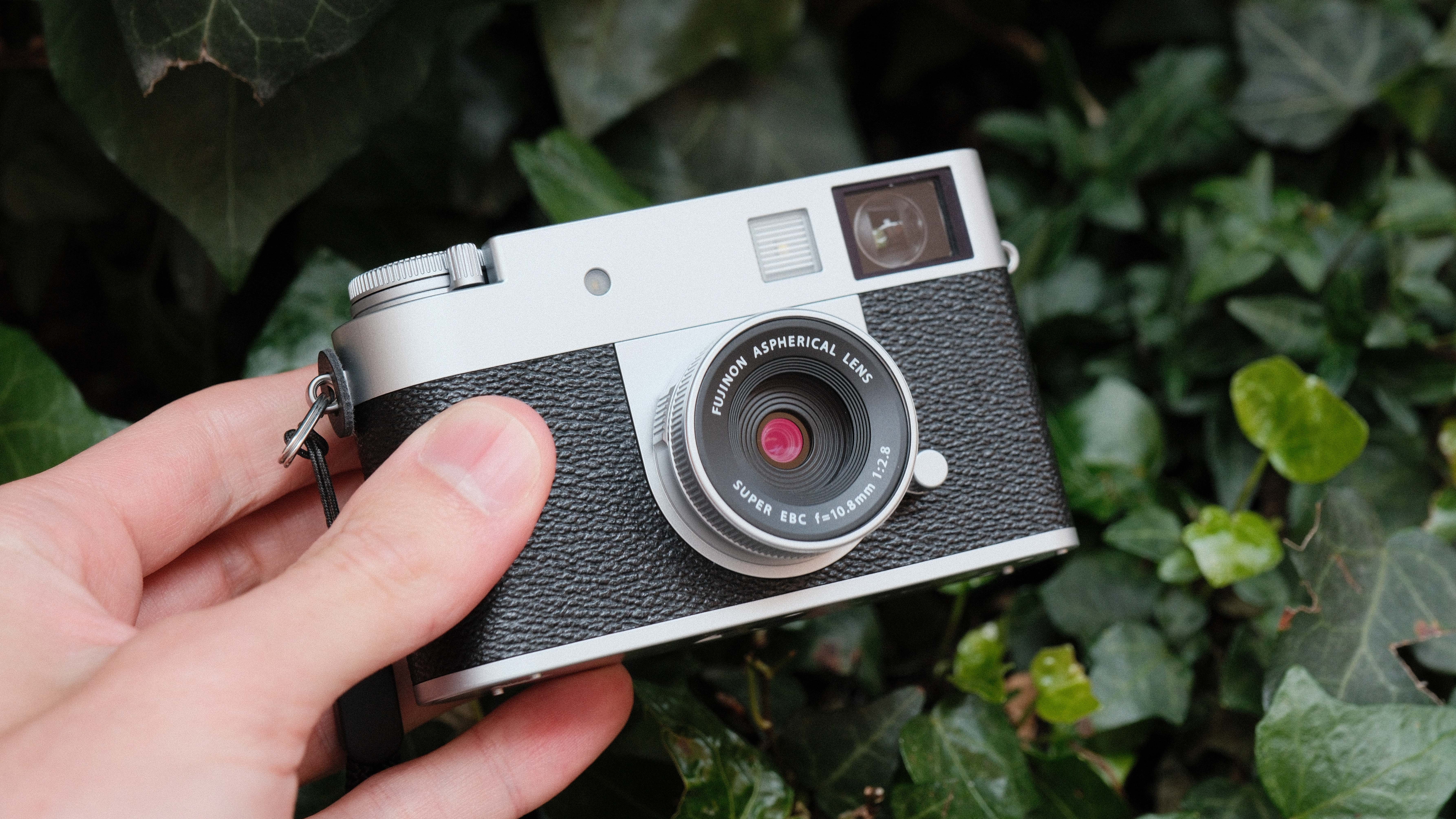 Fujifilm X Half camera held in a hand in front of some green leaves