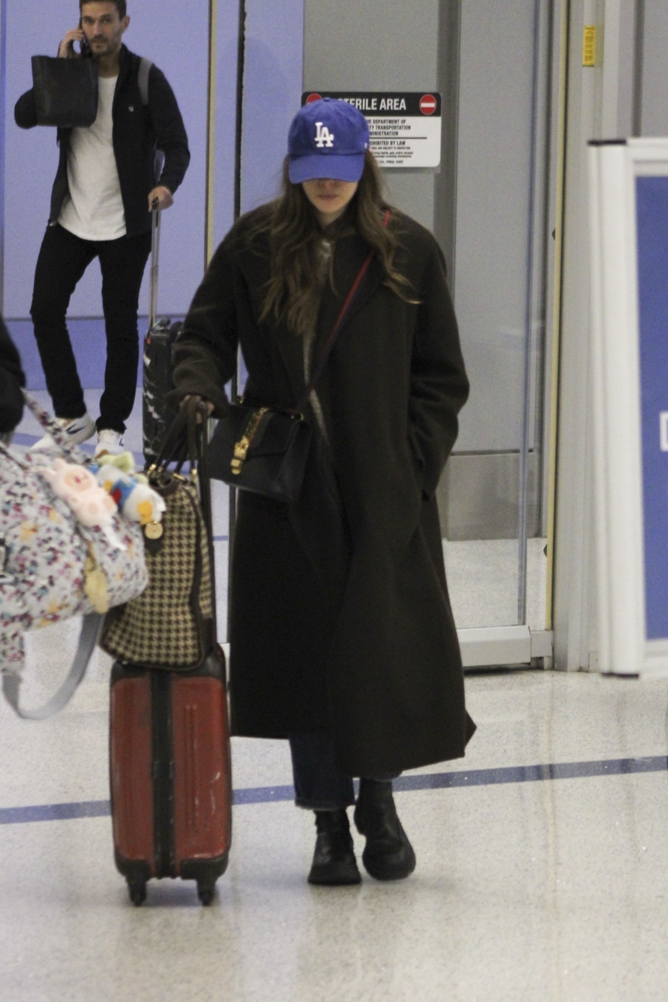 Elizabeth Olsen wears black boots with blue jeans, a black wool coat and a checked bag and cap.
