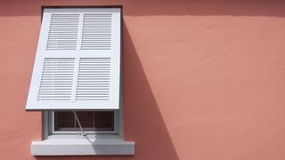 A storm shutter fitted to a window on a pink wall