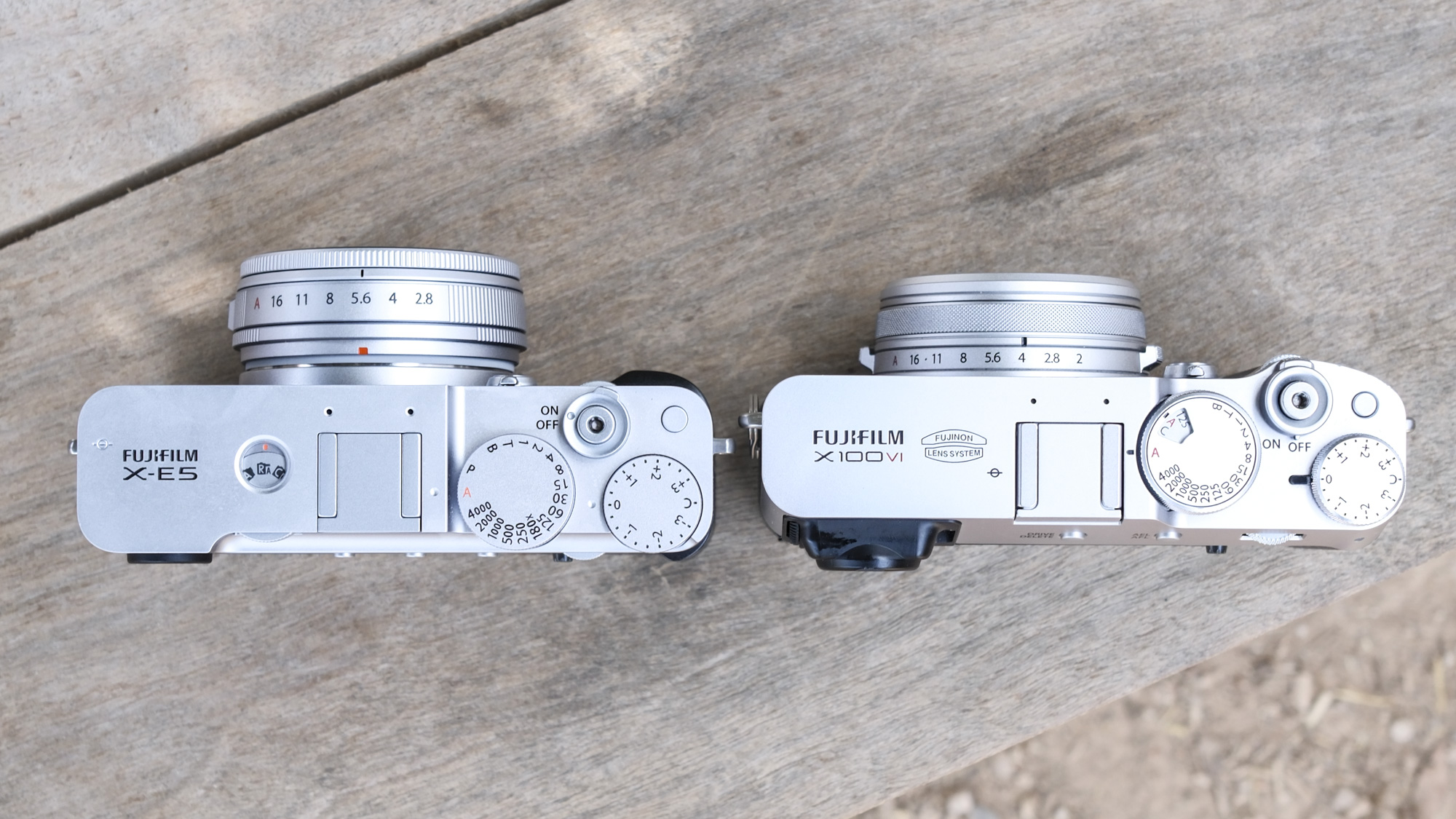 Top down of the Fujifilm X-E5 alongside the Fujifilm X100VI, on a wooden bench